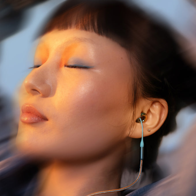 Person with their eyes closed wearing Loop x Coachella Experience 2 earplugs attached to a Loop x Coachella Link chord