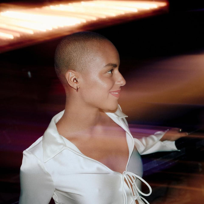 Woman in a white shirt with blurred lights in the background wearing Loop Switch 2 earplugs in gold