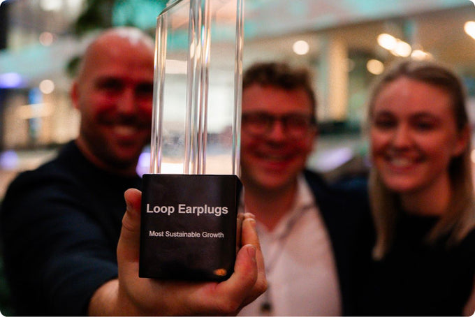 Person holding award for Most Sustainable Growth with a blurred background of three people