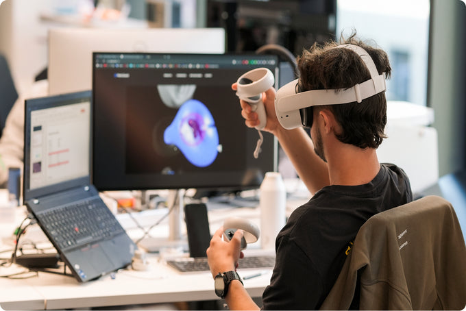 Person using a virtual reality headset in a modern office setting with multiple monitors and equipment.