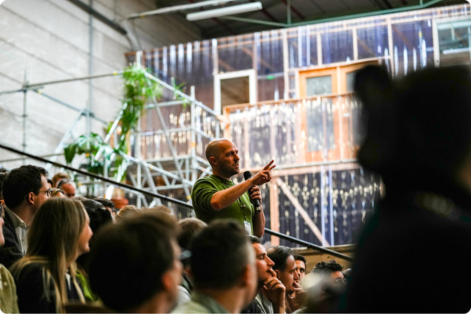 Man speaking into a microphone in front of an audience in a modern indoor setting.