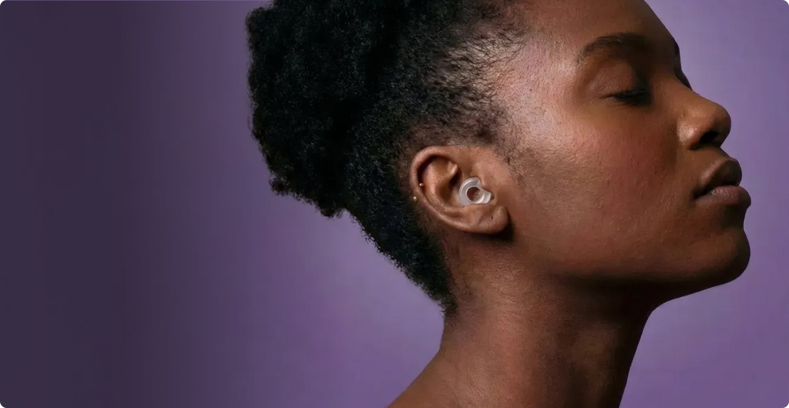 Close-up of a person wearing Loop Engage earplugs against a purple background