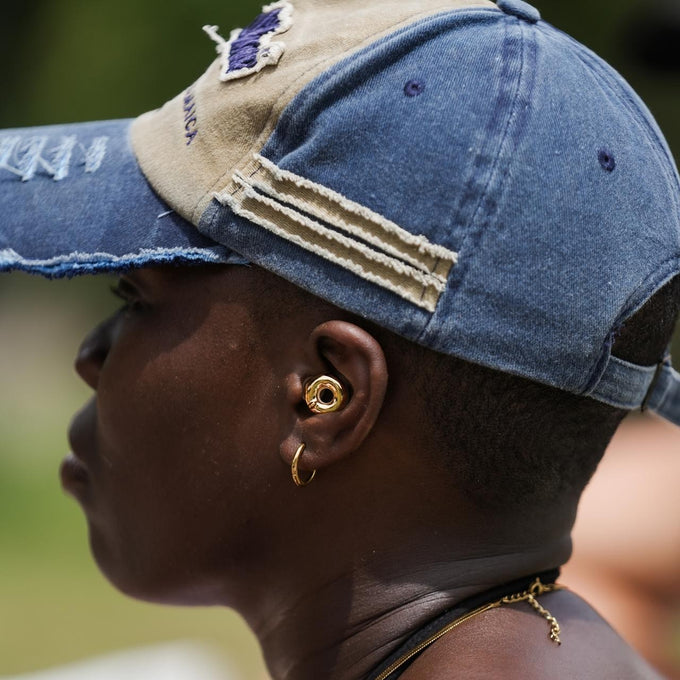 Person wearing a blue and beige cap and Loop Switch 2 earplugs in gold