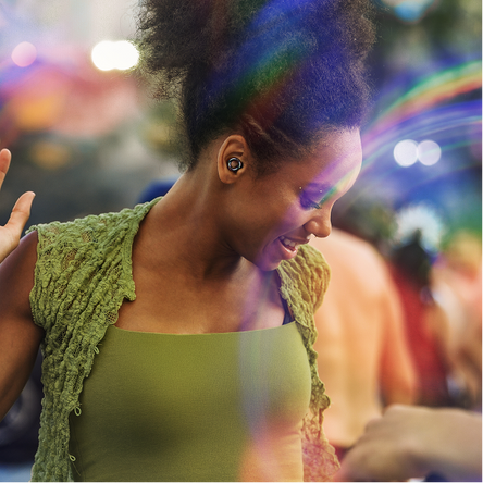 Woman dancing wearing a green top and green cardigan with a blurred festival background