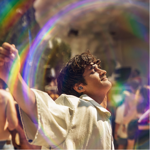 Person with a large bubble containing rainbow colors, surrounded by people in a festive setting.
