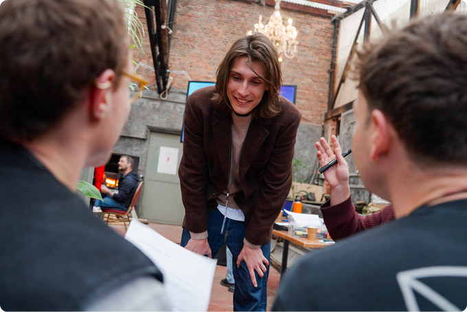 Two people interacting with a third person in an indoor setting with brick walls and furniture.